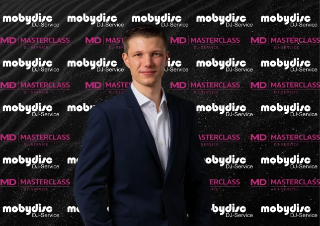 Junger Mobydisc Hochzeits-DJ im eleganten Anzug vor gebrandeter Eventwand