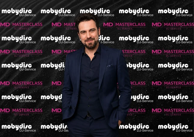 Eleganter Mobydisc Event-DJ im modernen Anzug vor professioneller DJ-Service Fotowand