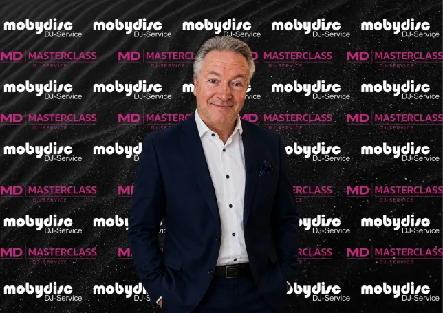 Stilvoll gekleideter Mobydisc DJ vor moderner Branding-Wand für Events