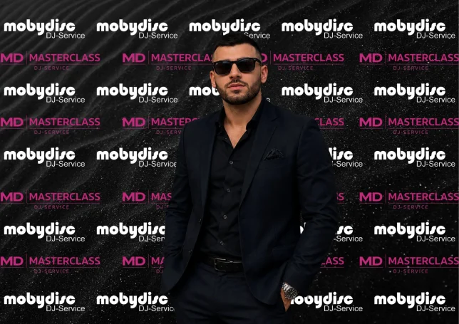 Moderner Event-DJ von Mobydisc DJ-Service im schwarzen Anzug vor Branding-Hintergrund