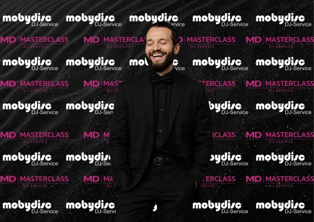 Eleganter Mobydisc DJ im schwarzen Anzug vor moderner Eventwand